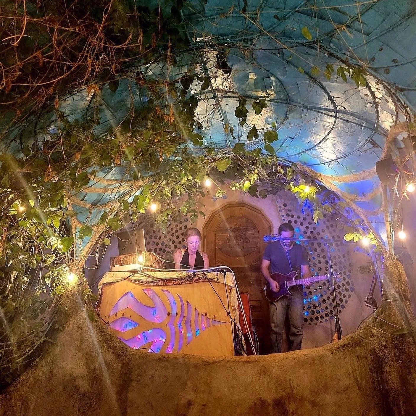 Silvermouse playing a candlelit show inside an earthship, under hanging vines and string lights